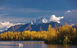 Una montaña con cima nevada, un lago con una embarcación y árboles de colores otoñales.