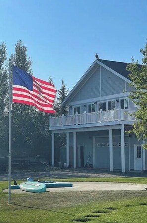 Un edificio de dos pisos con un balcón, un asta con la bandera estadounidense y un área verde con un kayak.