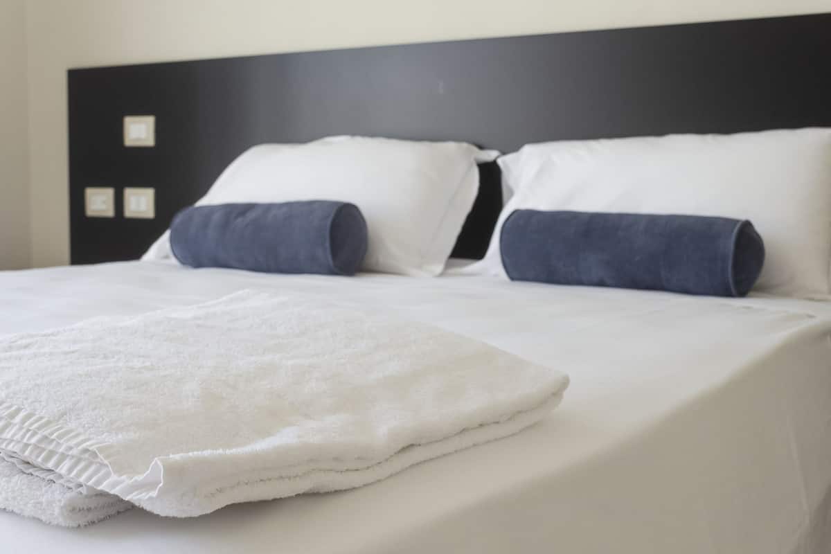 A neatly made bed with white bedding and two dark blue pillows, a white throw blanket, and a black headboard with a simple design.