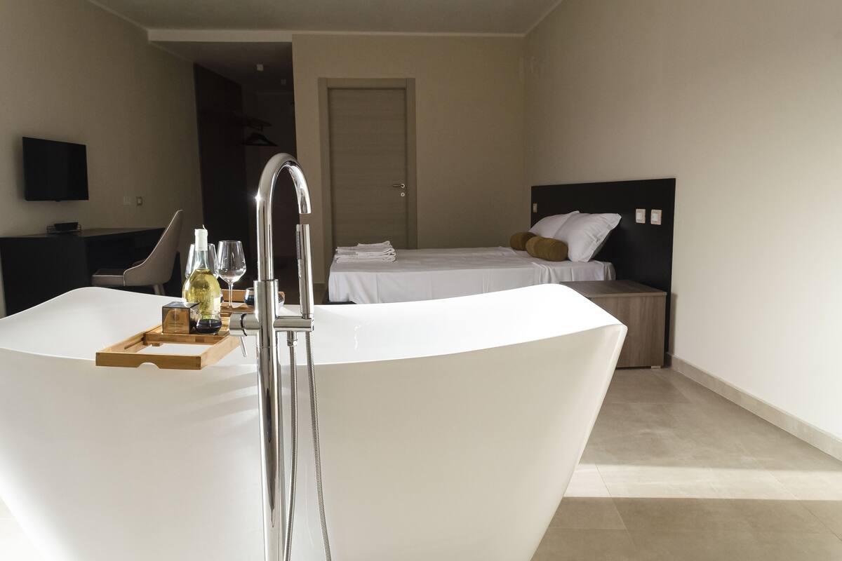 A modern bathroom with a large bathtub, a shower, and a bedside table with toiletries.