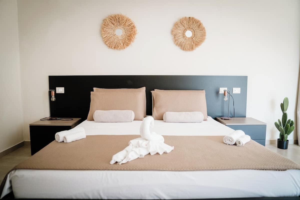 A hotel room with a large bed, two nightstands, a wall-mounted lamp, and a potted plant.