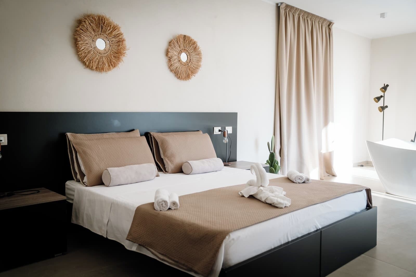 Habitació d'hotel moderna amb un llit gran, una tauleta de nit, una làmpada, una planta i una banyera.