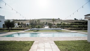 A swimming pool with a tiled pathway leading to it, surrounded by grass and palm trees. - DE MARE WINE RESORT (Ciro Marina)