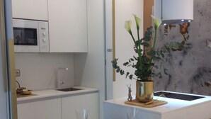 A modern kitchen with white cabinets, a microwave, and a sink. There is a dining area with a wooden table set for two, including plates, glasses, and cutlery. A vase with flowers is on the counter. - Apartment Boulevard luxury by Sebastiana Group (San Sebastián)