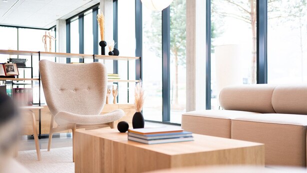 A modern living room with a beige armchair, a sofa, and a coffee table with books. - Coreum Hotel (Stockstadt am Rhein)