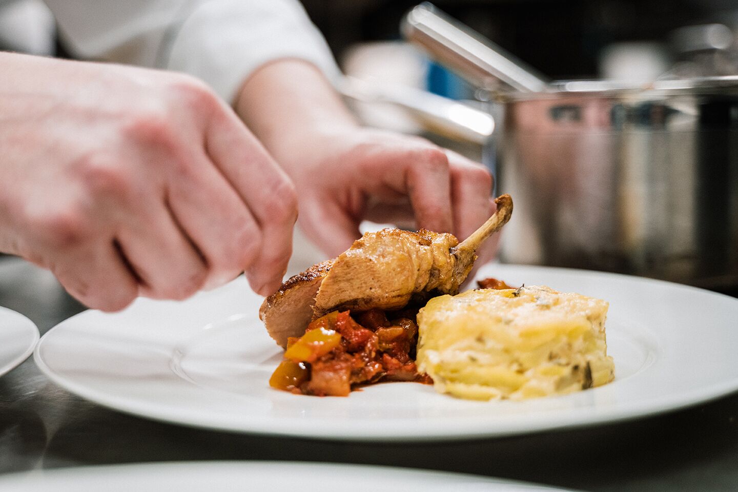 A chef preparing a dish with a roasted leg of lamb and a side of mashed potatoes.
