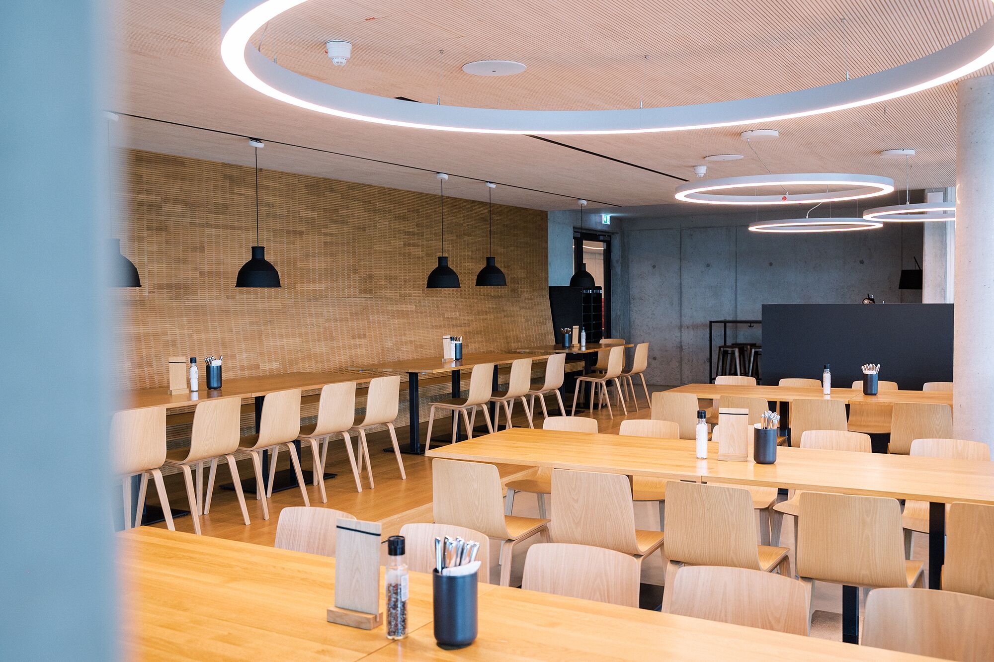 Una sala conferenze moderna con tavoli e sedie in legno, illuminazione a sospensione e una parete d'accento in legno.