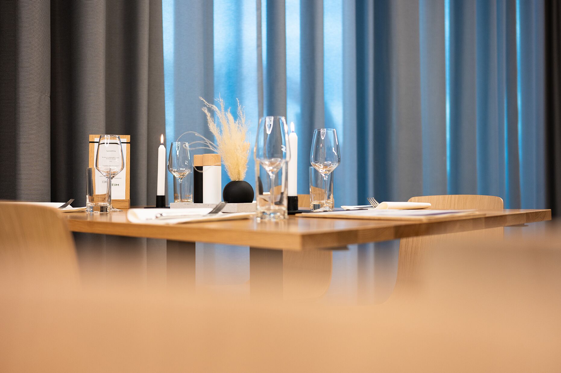 Uma mesa de jantar posta com taças de vinho, uma vela e um vaso com plantas secas.
