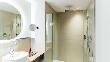 Un baño moderno con un espejo redondo, un lavabo blanco, una cabina de ducha de vidrio y un cabezal de ducha de mano.