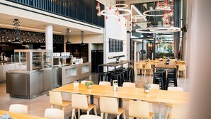 A modern restaurant with a central bar, multiple seating areas, and a high ceiling with hanging light fixtures. - Coreum Hotel (Stockstadt am Rhein)
