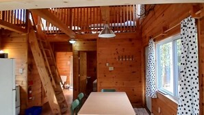 L’intérieur d’un chalet en bois, avec une table à manger, des chaises, un escalier et une fenêtre avec des rideaux.
