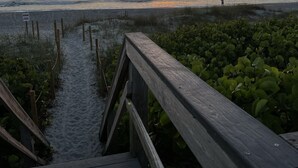 Une promenade en bois menant à une plage, avec un coucher de soleil en arrière-plan.