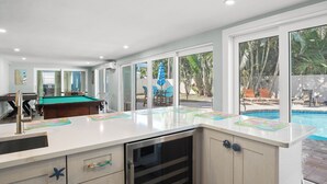 Une cuisine moderne dotée d’une table de billard intégrée, d’un lave-vaisselle et d’une grande fenêtre donnant sur une piscine.