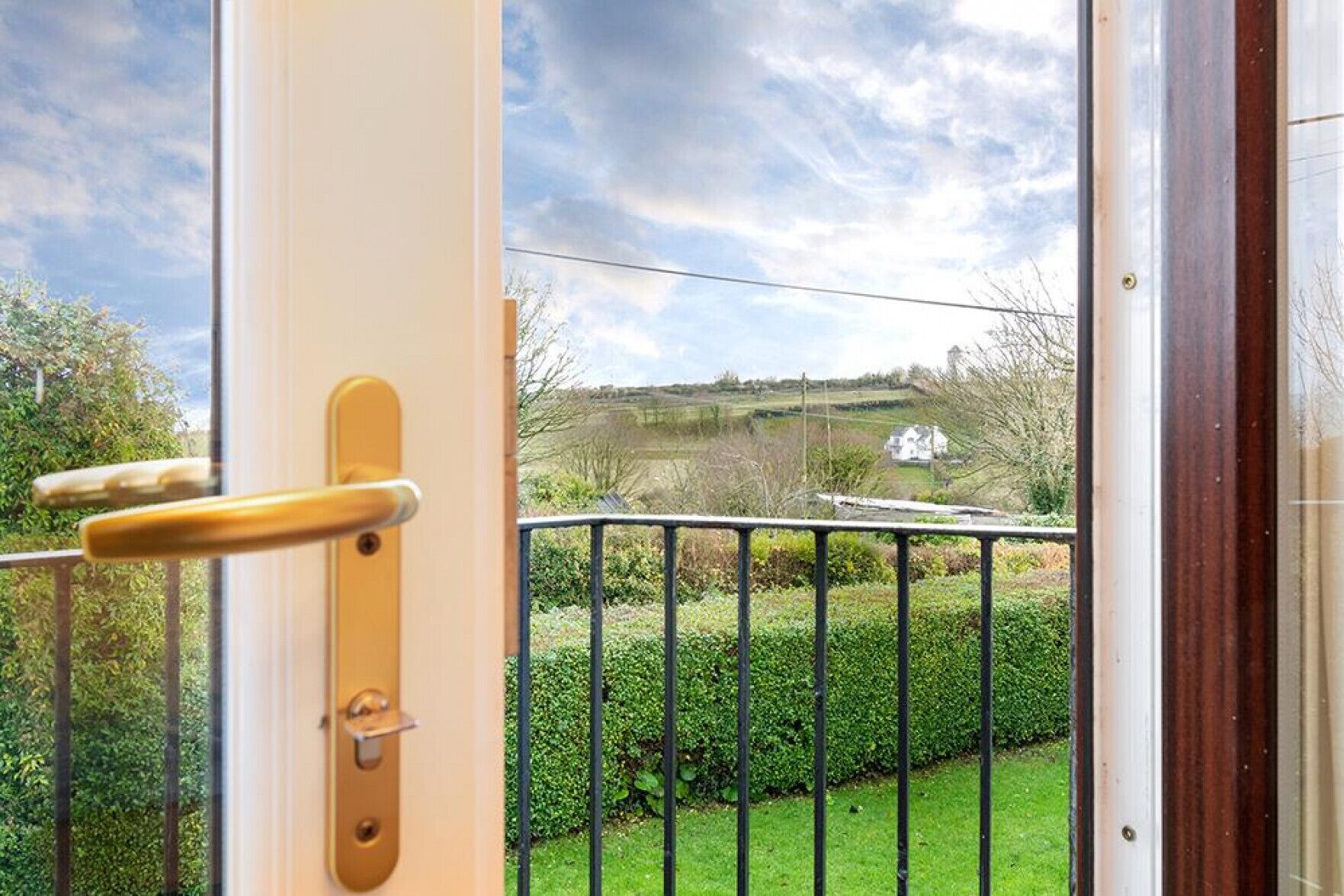 Ein Balkon mit Blick auf eine ländliche Landschaft, einem Metallgeländer und einer Tür mit Griff.