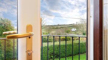 Ein Balkon mit Blick auf eine ländliche Landschaft, einem Metallgeländer und einer Tür mit Griff.