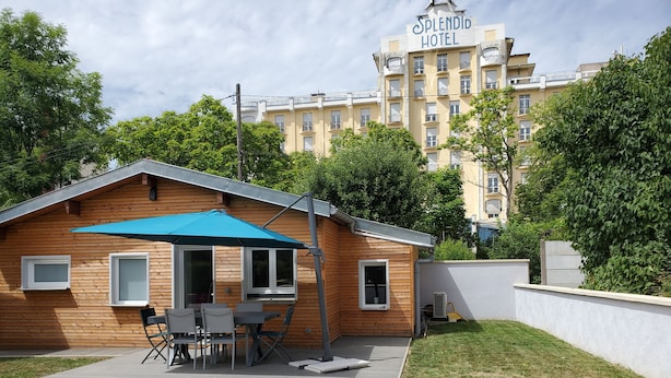 Una cabaña de madera con toldo azul, una mesa y sillas, con un edificio de hotel de fondo.