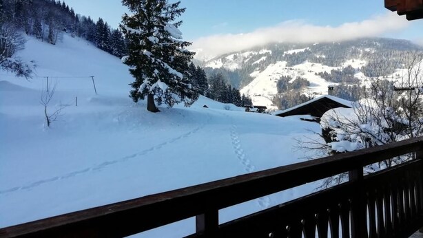 Een besneeuwd berglandschap met een houten terras en een chalet op de achtergrond.