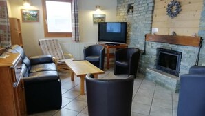 Een gemeubileerde woonkamer met een bank, fauteuils, een salontafel, een televisie en een open haard.