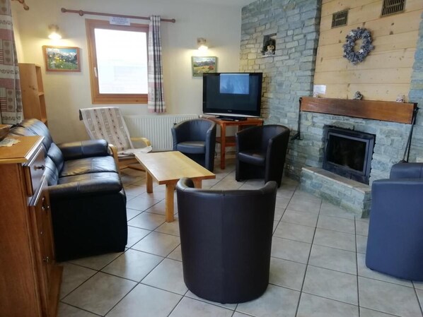 A furnished living room with a sofa, armchairs, a coffee table, a television, and a fireplace. - Chalet, parking, TV, 130 m², Arêches-Beaufort (Beaufort)