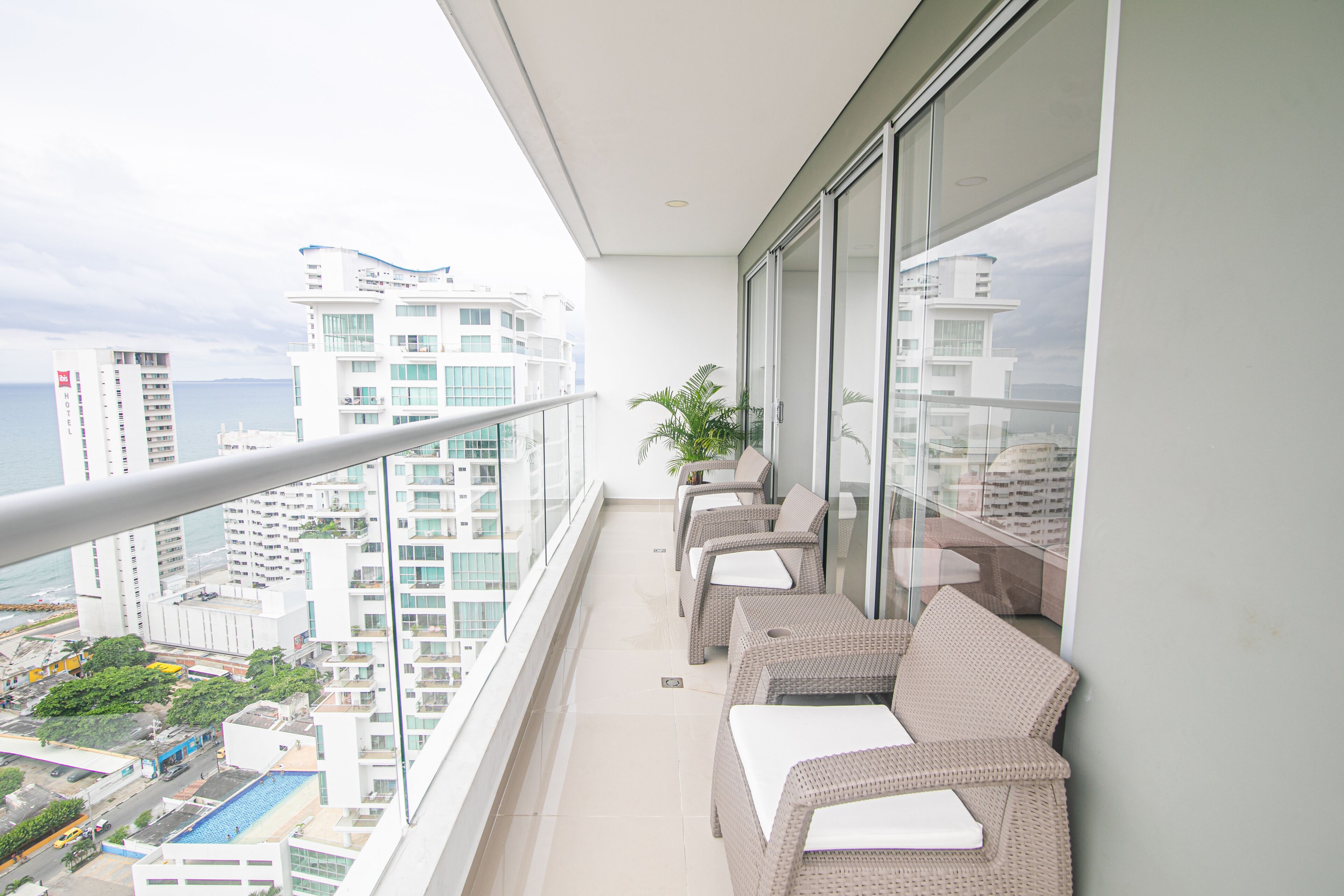 A balcony with wicker furniture, a glass railing, and a view of the cityscape and ocean.