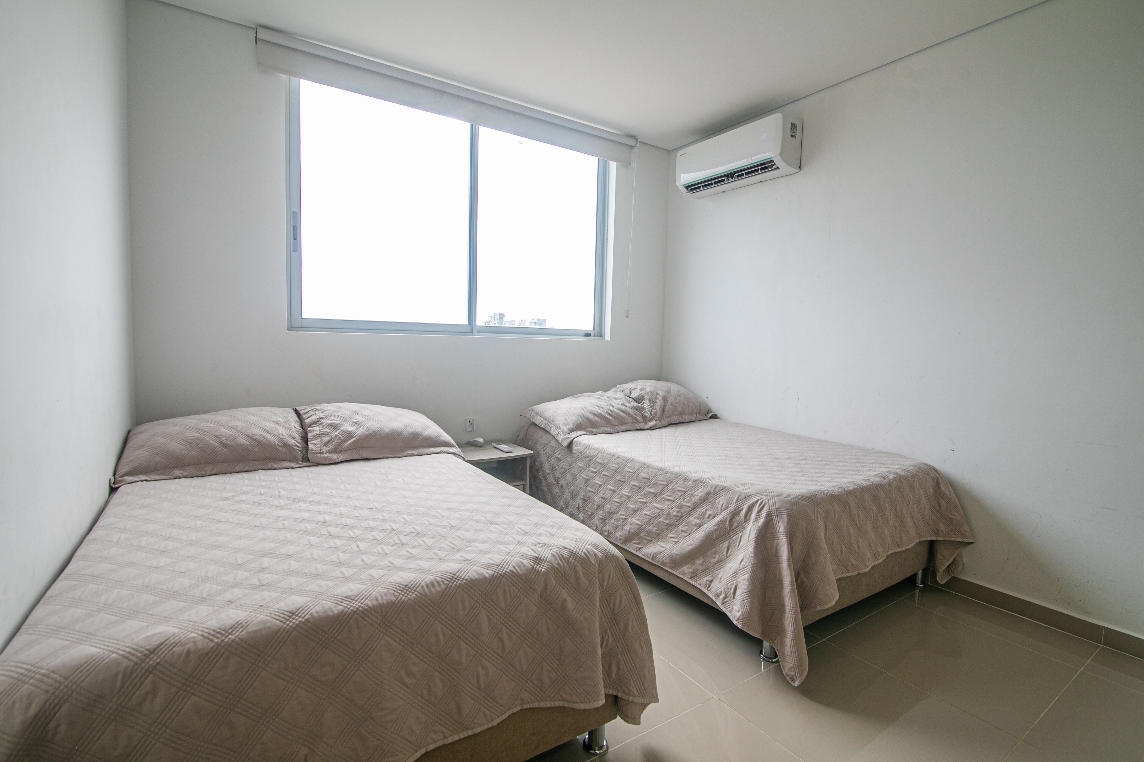A room with two beds, a window, and an air conditioning unit.