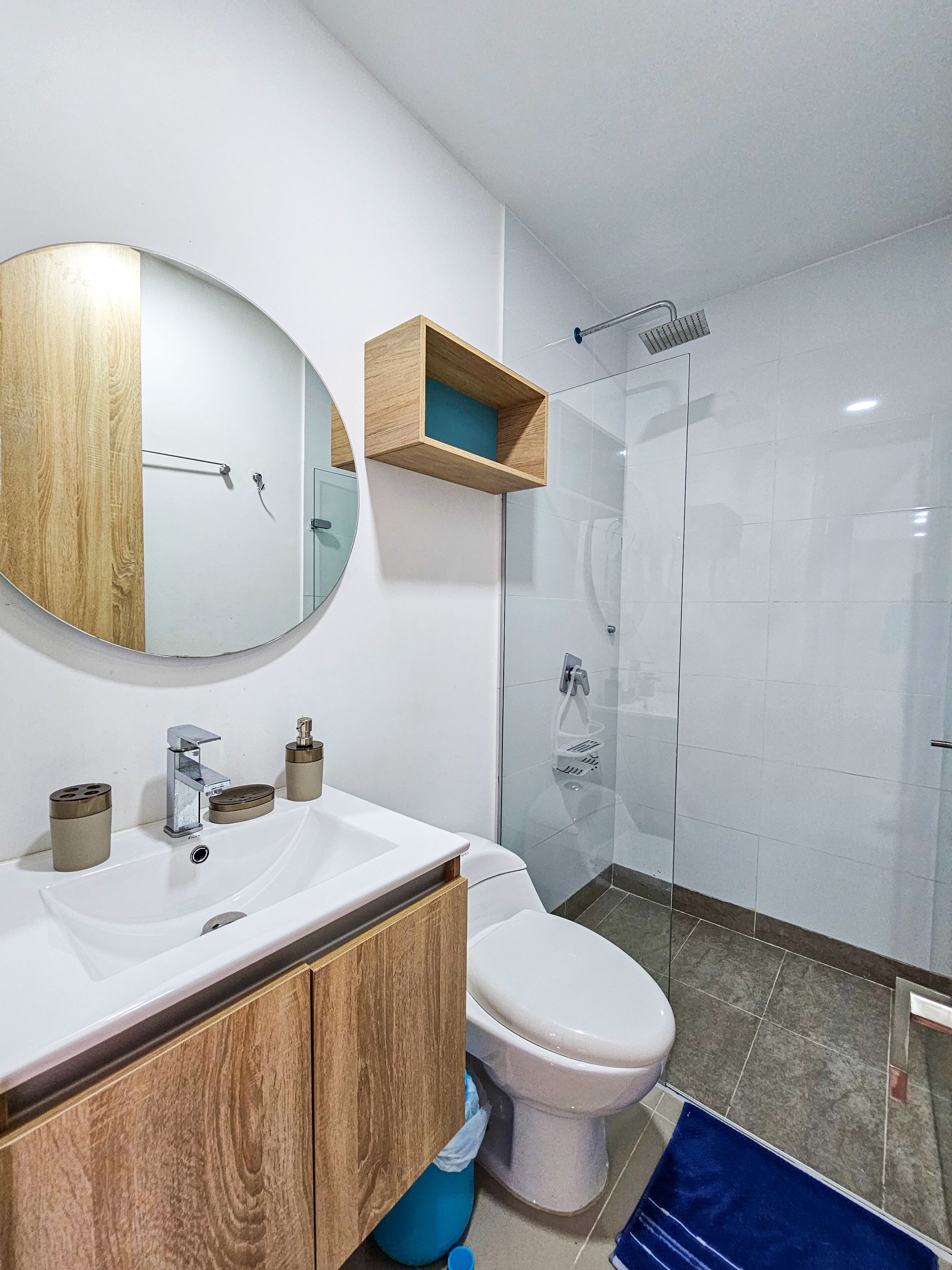 Un bany modern amb un lavabo blanc, un mirall, un vàter i una dutxa amb envàs de vidre.