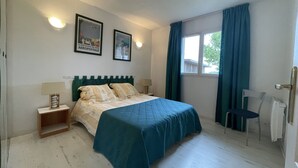 Ein Schlafzimmer mit einem Bett, zwei Wandleuchten, einem Fenster mit Vorhängen und zwei gerahmten Bildern an der Wand.