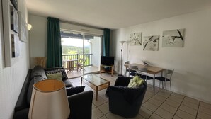Ein Wohnzimmer mit einer Couch, einem Couchtisch und Sesseln, ein Balkon mit Tisch und Stühlen, sowie Kunstwerke an den Wänden.