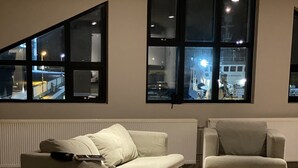 Ein modernes Wohnzimmer mit zwei Sofas und einem Sessel, großen Fenstern mit Blick auf die Stadt und einer Heizung unter den Fenstern.