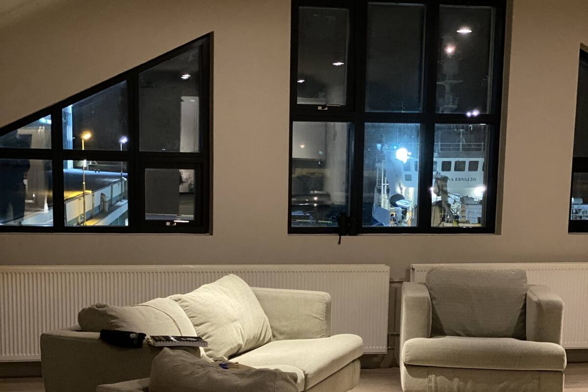 A modern living room with two sofas and a chair, large windows with city views, and a radiator under the windows.