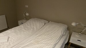 Ein Zimmer mit einem Einzelbett, weißer Bettwäsche, zwei Nachttischen mit Lampen und einem Heizkörper links.