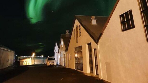 Eine Straße mit Häusern unter einem Nachthimmel mit grünem Polarlicht.