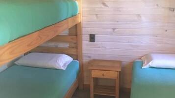 A small, cozy room with two bunk beds and a single bed, wooden walls, and a small wooden nightstand.