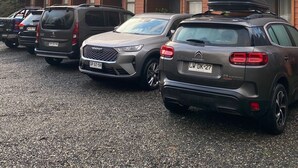 Fila de cotxes aparcats davant d'un edifici amb moltes finestres i un teulat inclinat.