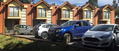 A row of red brick townhouses with multiple cars parked in front.