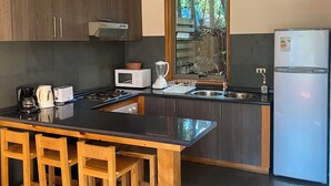 Una cuina moderna amb una illa central, tamborets de fusta, armaris fosc, un rentaplatets d'acer inoxidable i un microones integrat.