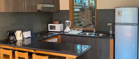 Una cocina moderna con una isla central, taburetes de bar de madera, armarios oscuros, un lavaplatos de acero inoxidable y un microondas integrado.