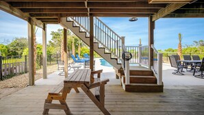 Une terrasse en bois avec un escalier menant à un espace abrité, un coin salon extérieur et une piscine.