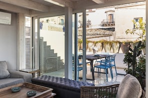 A modern living room with a sofa, a dining table with chairs, and a view of the street through large glass doors.