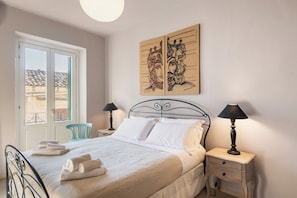A bedroom with a bed, two bedside tables with lamps, a window with a view, and artwork on the wall.
