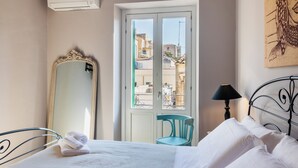 Ein Hotelzimmer mit einem Bett, einem Sessel, einem großen Spiegel, einer Lampe und Blick durch eine Tür.