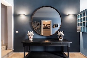 A dark blue wall with a round mirror, two decorative busts, and a small clock.