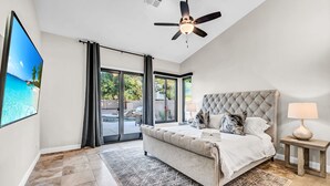Une chambre dotée d’un grand lit, d’un ventilateur de plafond, d’une télévision et offrant une vue sur une piscine et la verdure environnante.