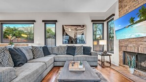 Un salon moderne avec un canapé d’angle, une cheminée et de grandes fenêtres donnant sur l’extérieur.