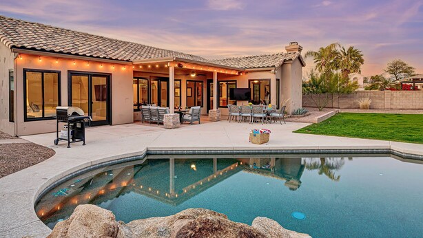 Une maison avec une piscine, du mobilier de jardin et un espace barbecue.