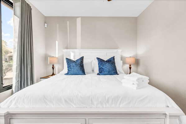 A neatly made bed with white linens, two blue pillows, and a white headboard.