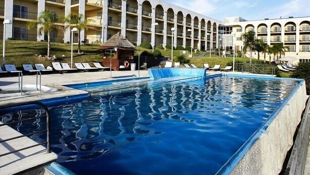 A hotel with a large pool, sun loungers, and a building with multiple balconies.