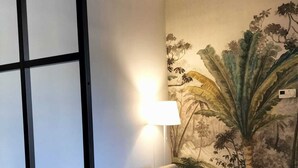 Et værelse med en grå sofa, en skillevæg med sort ramme og en væg med et blomstermotiv.