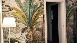 Et værelse med et muralmaleri af tropisk vegetation på væggen, en sofa og en lampe.