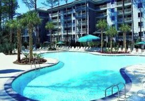 Relax by the resort pool surrounded by palm trees and lounge chairs.